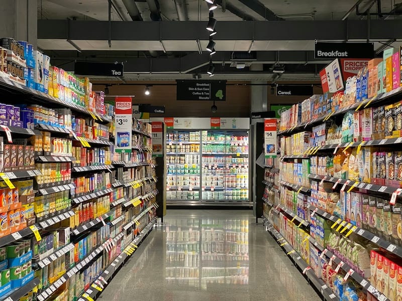 A photo of a supermarket isle with products on both sides and a dairy cooler at the end